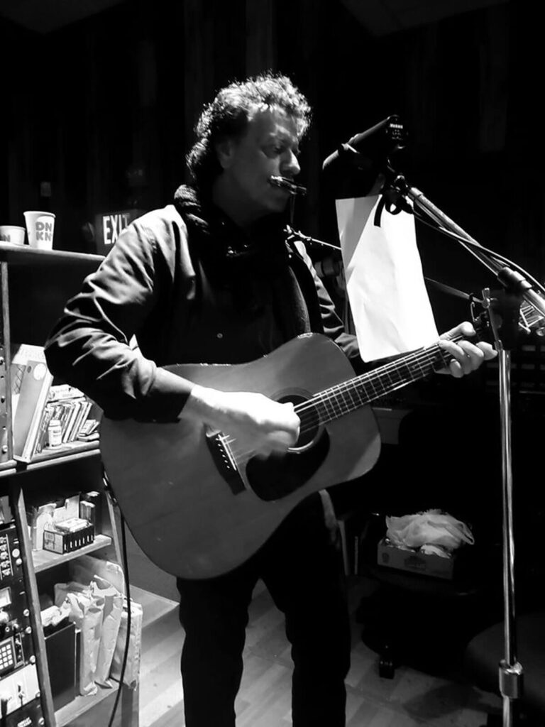 Steven Keene, inventor of HarMotion, singing at the microphone with an acoustic guitar